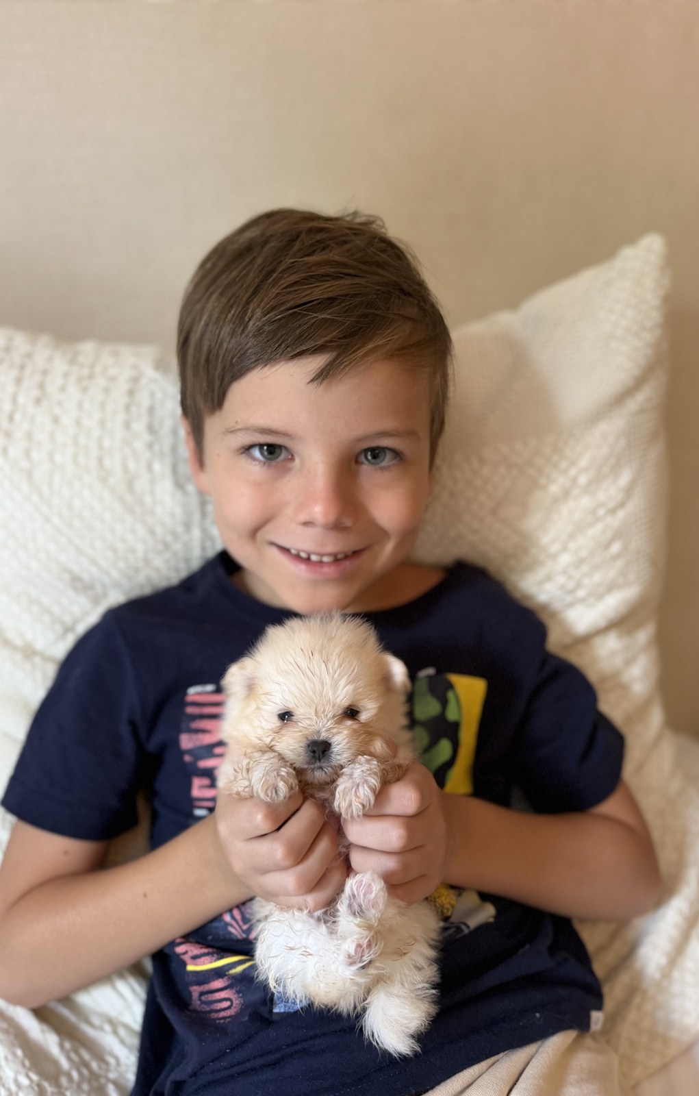 Our son smiling with a cream Pomeranian puppy